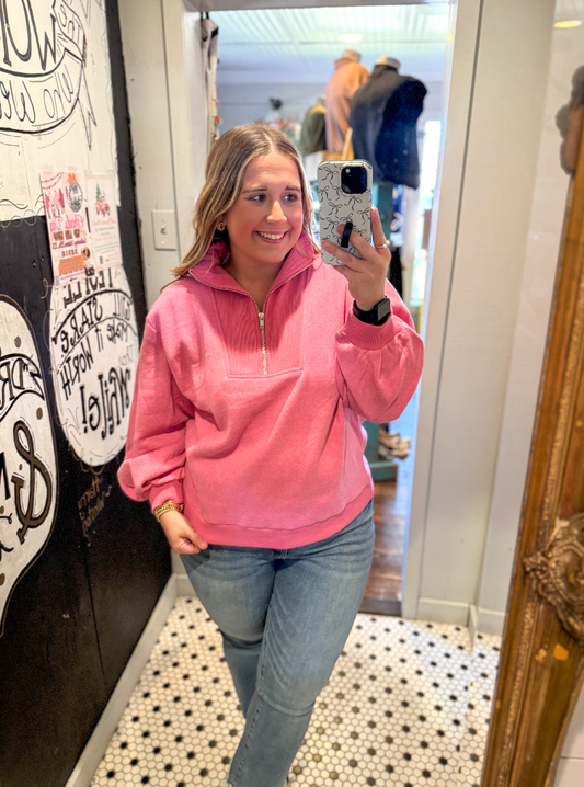 Woman taking a mirror selfie wearing a pink pullover and blue jeans in a store.