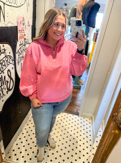 Woman taking a mirror selfie wearing a pink pullover and blue jeans.