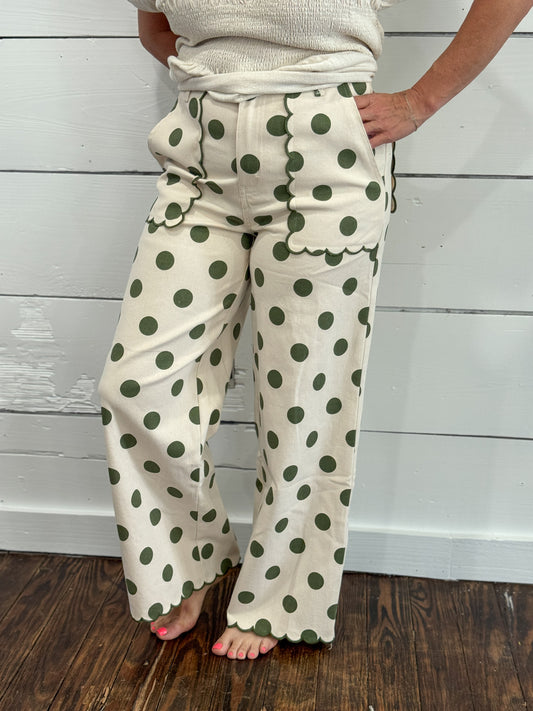 A person wearing cream wide-leg pants with dark green polka dots, standing barefoot on a dark wood floor against a white shiplap wall.