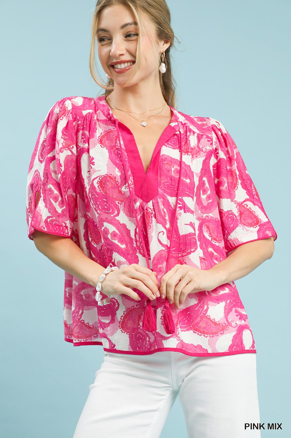 Woman wearing a pink and white patterned blouse against a light blue background