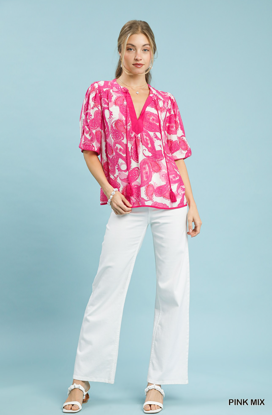 Woman wearing a pink floral blouse and white pants on a light blue background