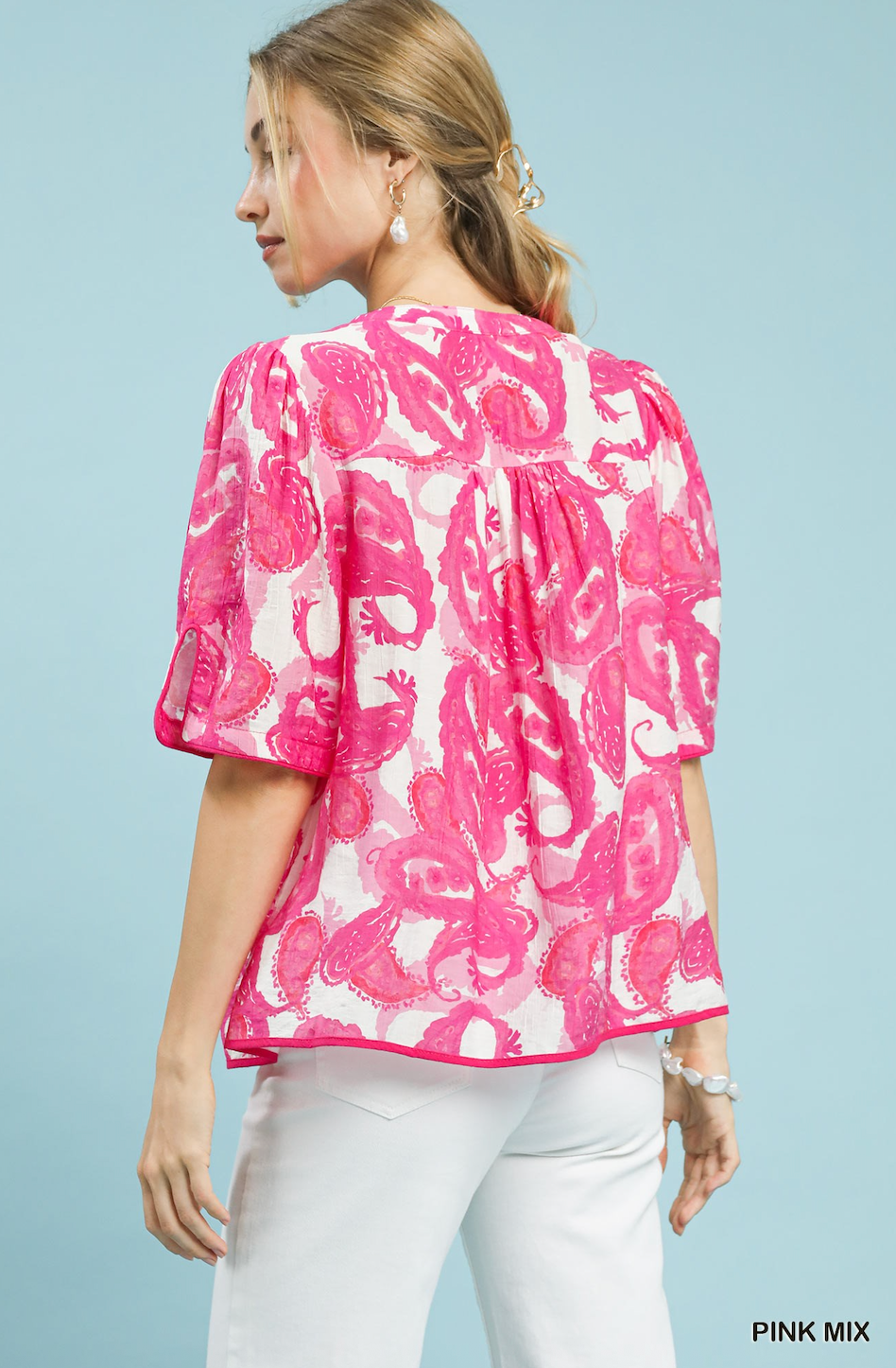 Woman wearing a pink floral blouse with white pants against a light blue background