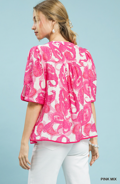 Woman wearing a pink floral blouse with white pants against a light blue background