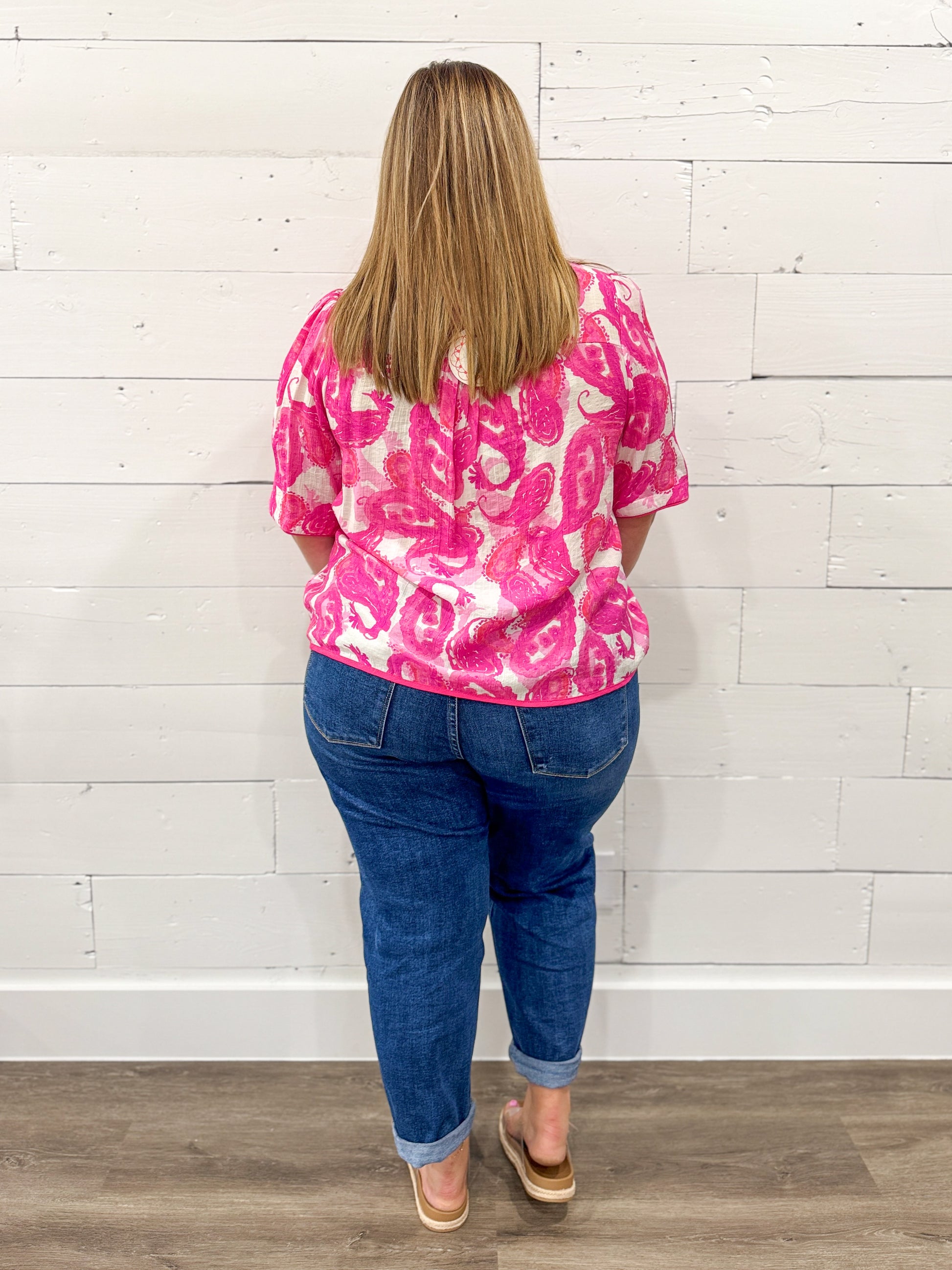 Person wearing a pink and white patterned shirt and blue jeans against a white wooden panel background