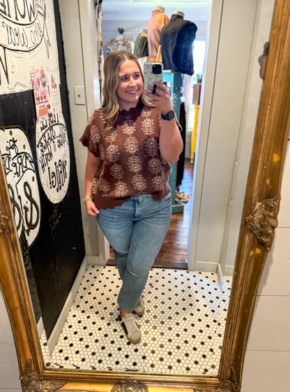 Woman taking a mirror selfie wearing a brown patterned sweater and blue jeans in a store.