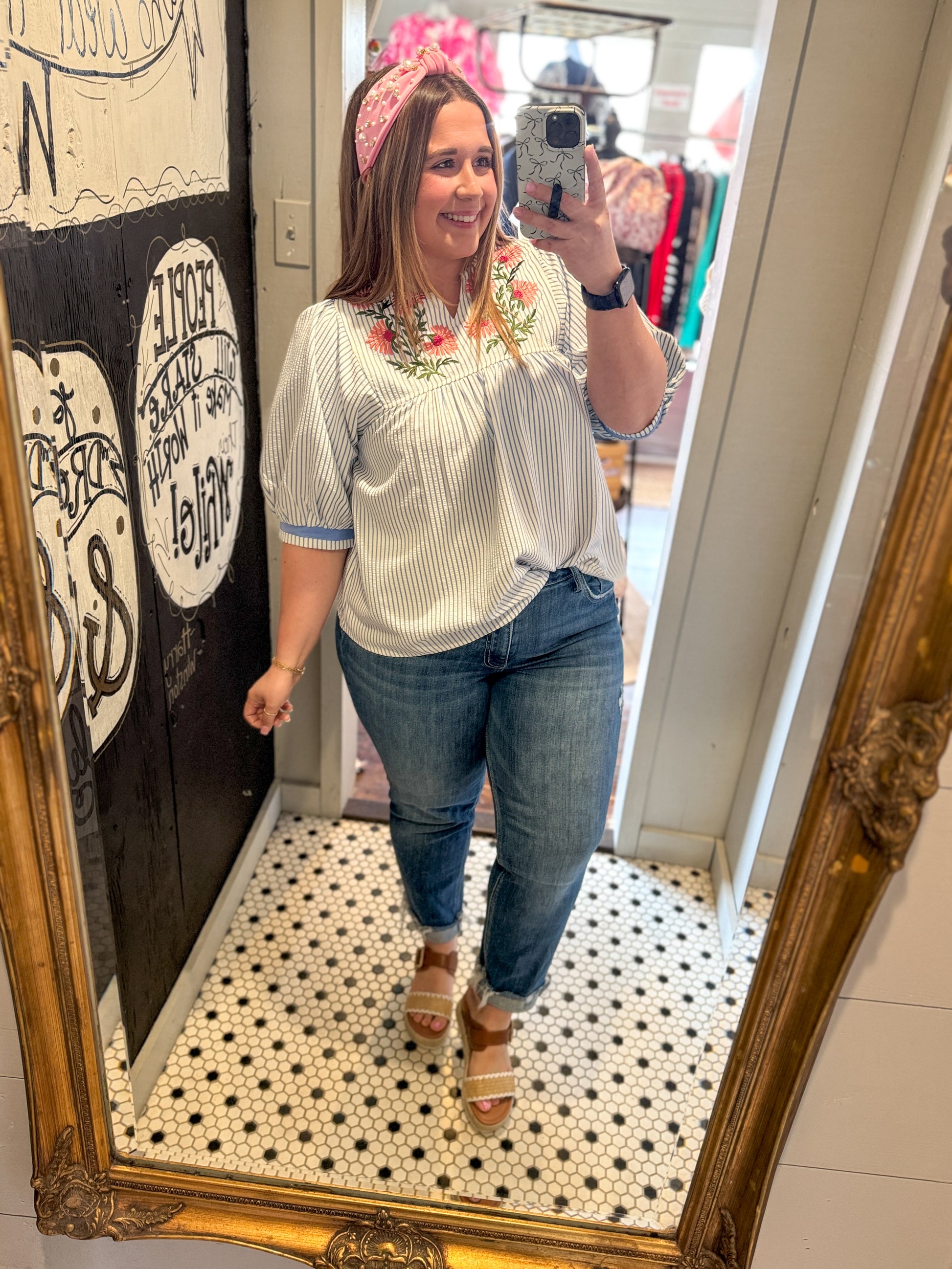 Woman taking a mirror selfie wearing a striped shirt and jeans in a store.