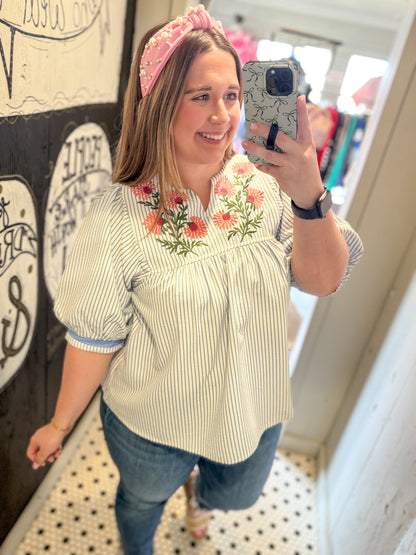 Woman taking a mirror selfie wearing a floral embroidered blouse and pink headband.
