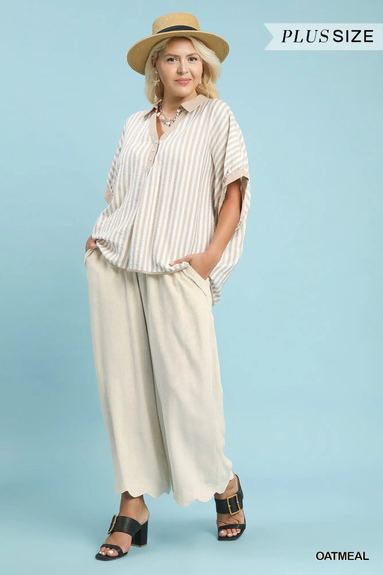 Woman wearing a striped blouse and wide-leg pants with a straw hat on a light blue background.