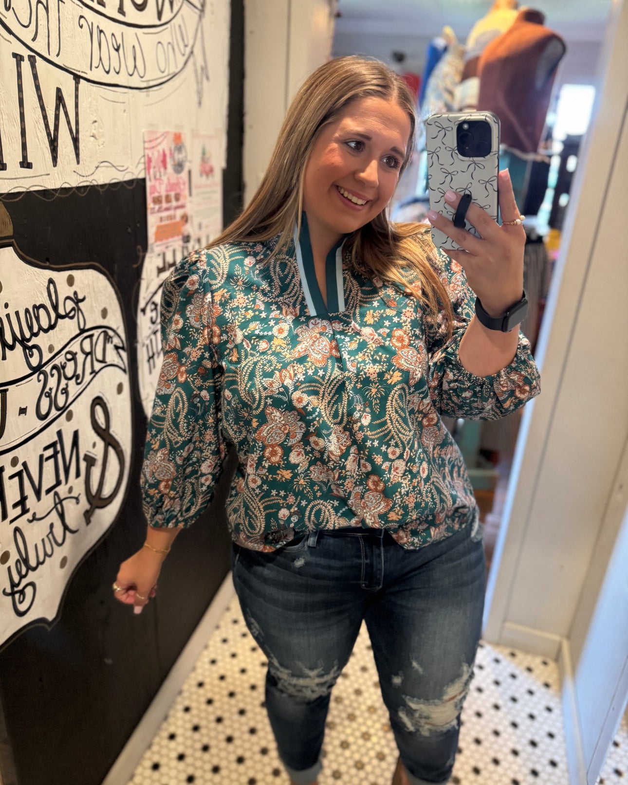 Woman taking a mirror selfie wearing a floral blouse and jeans in a store.
