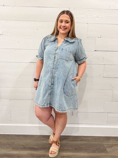 Woman wearing a light blue denim dress with  a plain background