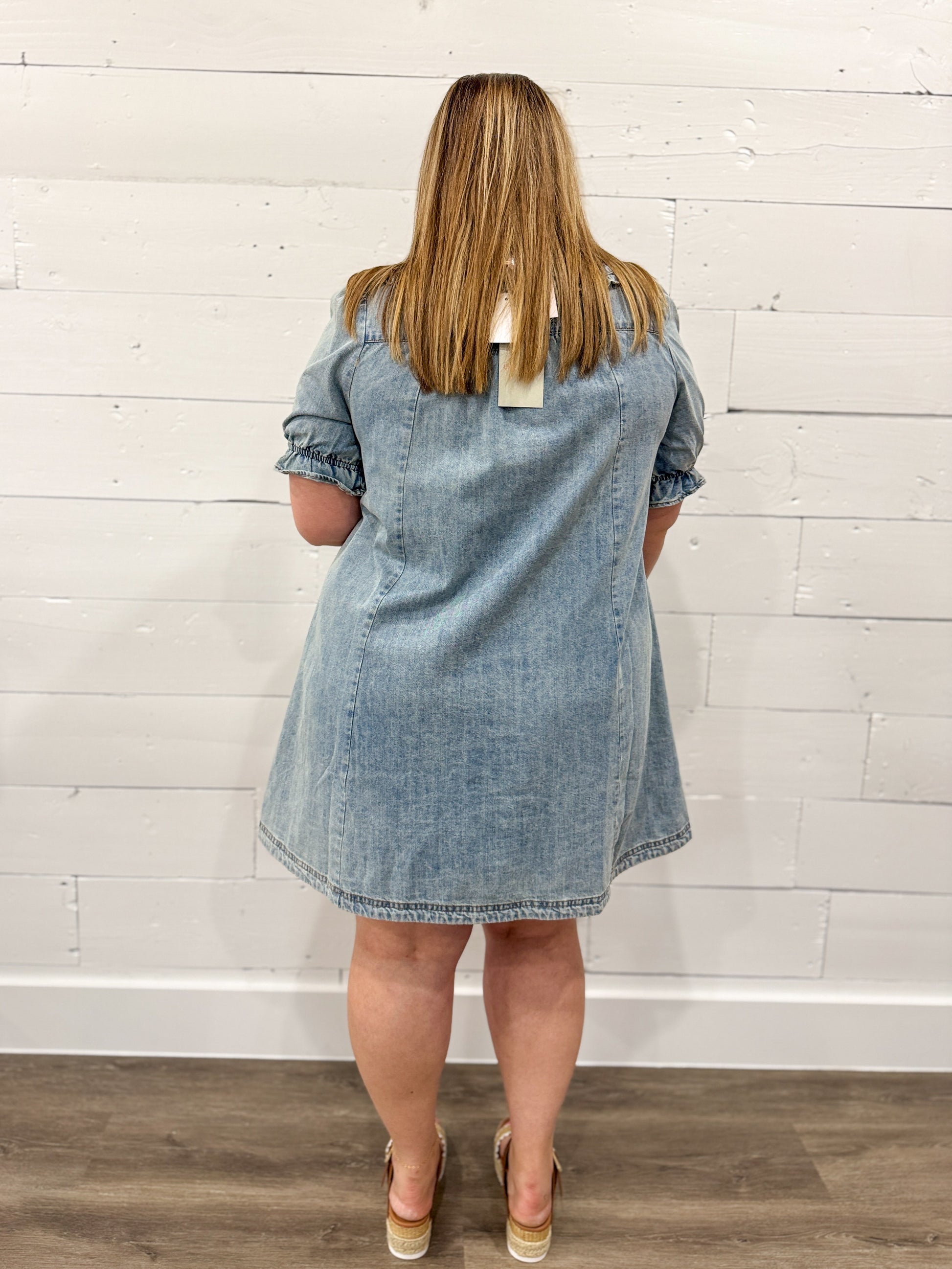 Woman wearing a light blue denim dress with  a plain background