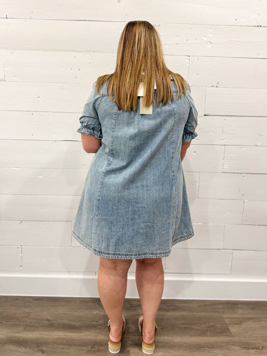 Woman wearing a light blue denim dress with  a plain background