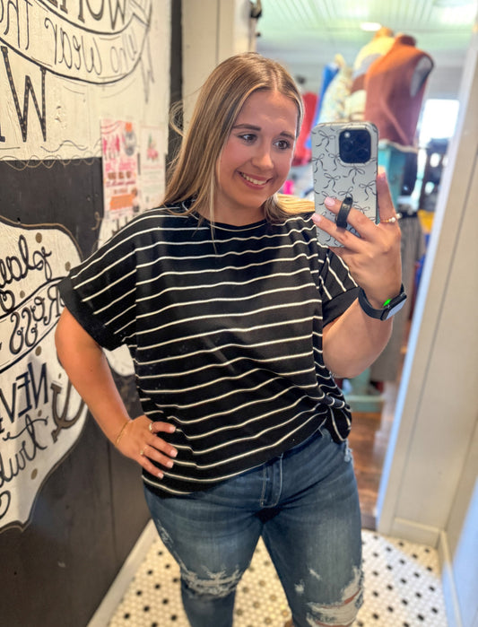 Woman taking a mirror selfie wearing a striped shirt and jeans in an indoor setting.