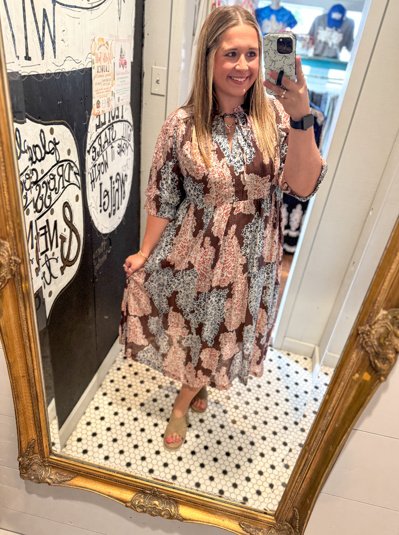 Woman taking a mirror selfie wearing a patterned dress in a store.