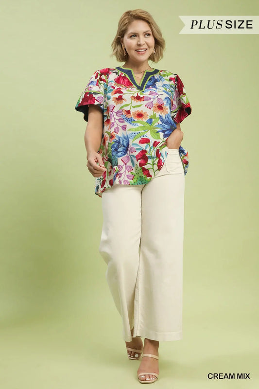 Woman wearing a colorful floral blouse and cream pants on a light green background