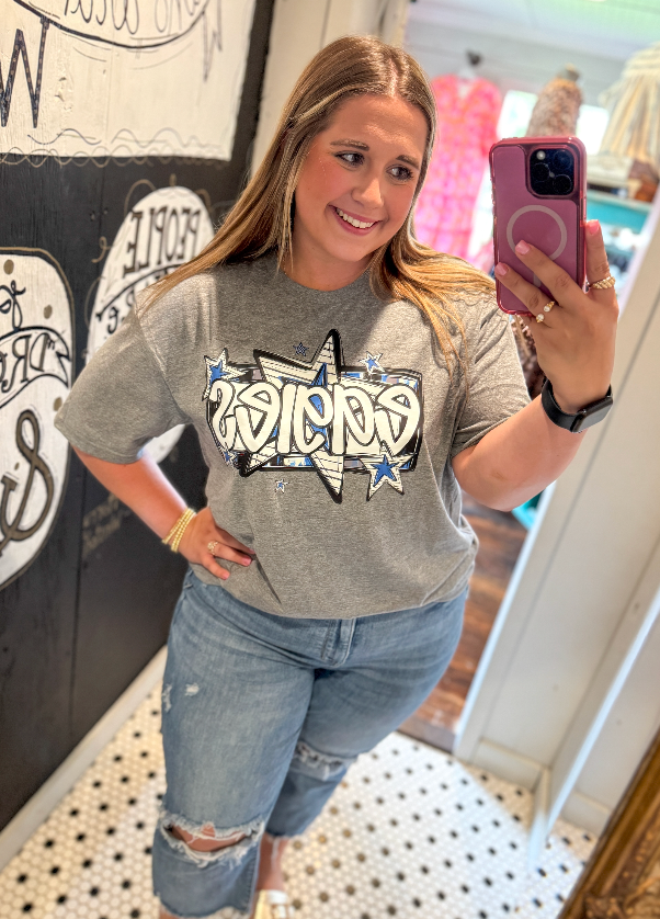 Woman taking a selfie wearing a gray t-shirt with a graphic design, standing in a room with decorative elements.