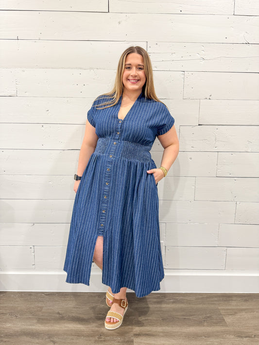 Woman wearing a blue striped dress standing against a white brick wall.