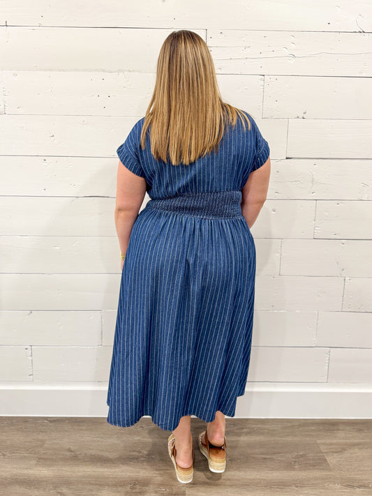 Woman wearing a blue striped dress standing against a white brick wall.