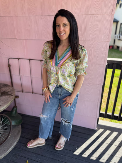 Woman wearing a floral blouse and jeans standing on a porch.