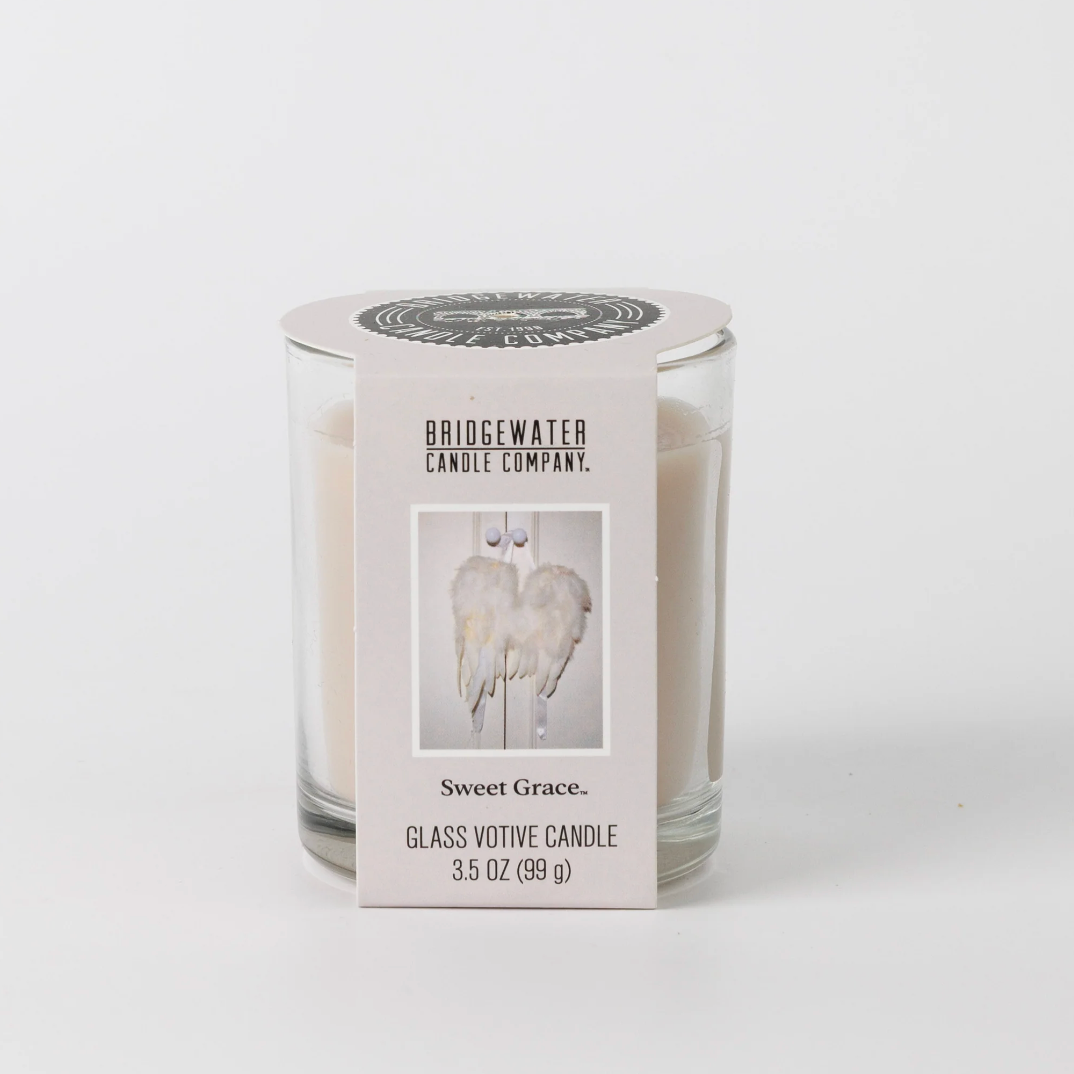A glass votive candle in a clear glass jar with a white paper label. The label reads 'BRIDGEWATER CANDLE COMPANY' and 'Sweet Grace.