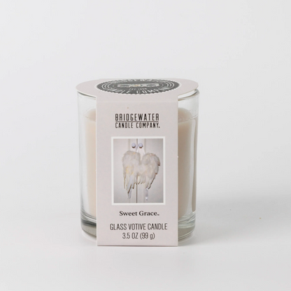 A glass votive candle in a clear glass jar with a white paper label. The label reads 'BRIDGEWATER CANDLE COMPANY' and 'Sweet Grace.