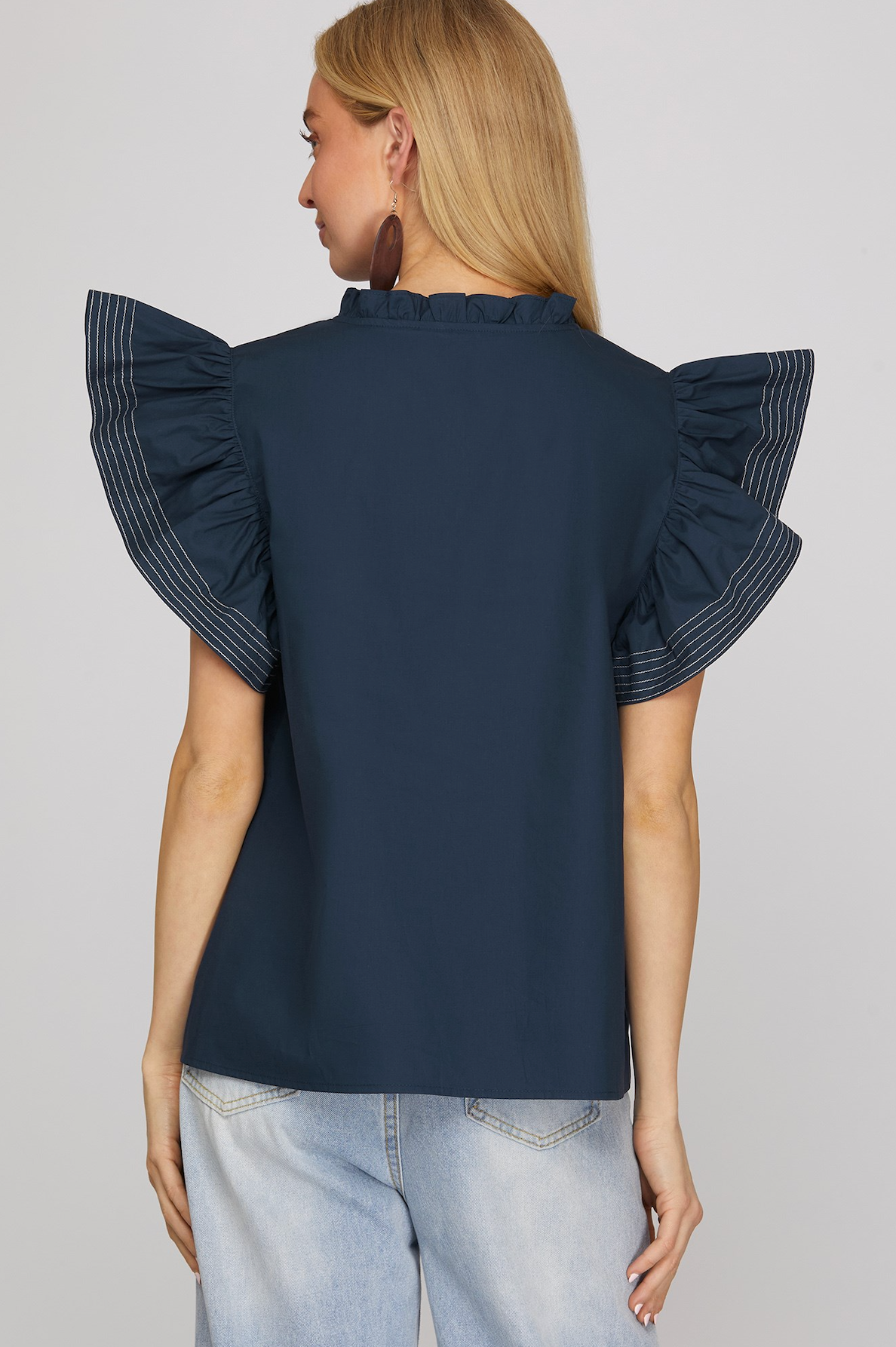 Navy blue blouse with ruffled sleeves worn by a person on a light gray background
