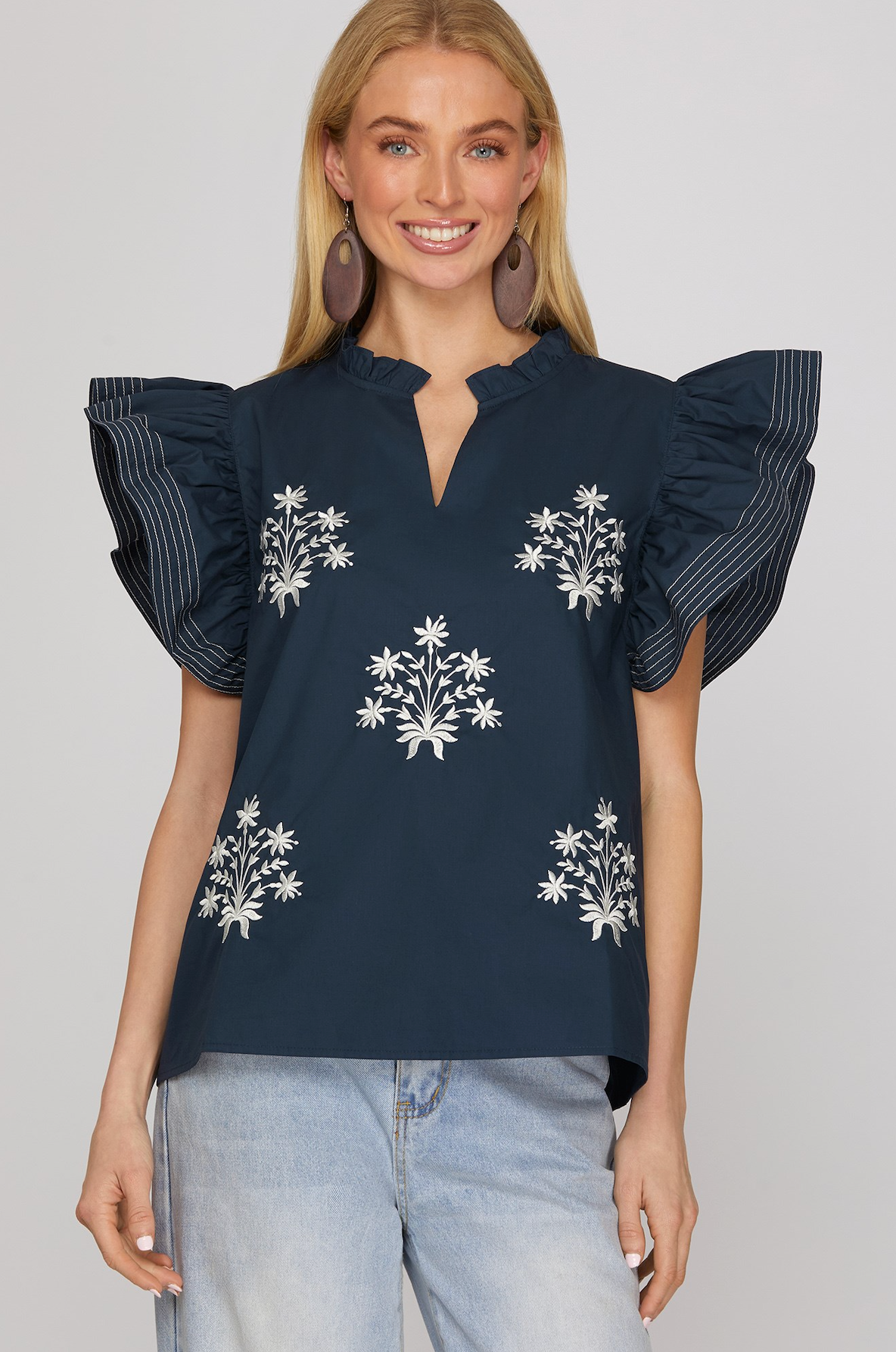 Woman wearing a navy blue blouse with floral embroidery and ruffled sleeves on a white background