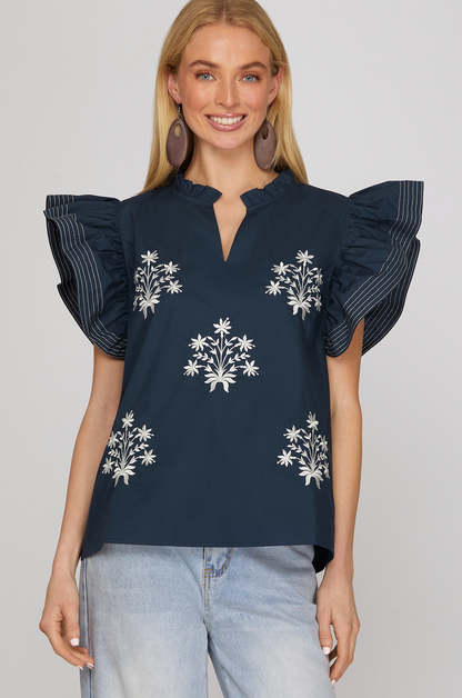 Woman wearing a navy blue blouse with floral embroidery and ruffled sleeves on a white background