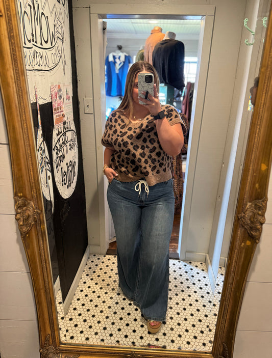 Person taking a mirror selfie wearing a leopard print top and blue jeans in a store.