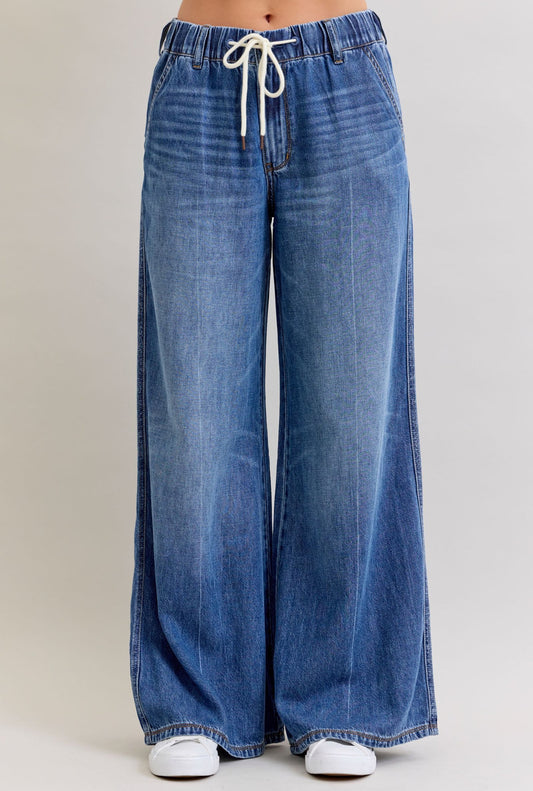 Blue wide-leg jeans with a drawstring waist on a beige background