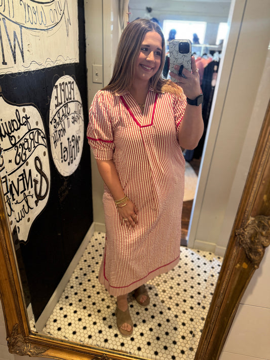 Woman taking a mirror selfie wearing a pink dress with red trim in a room with decorative elements.