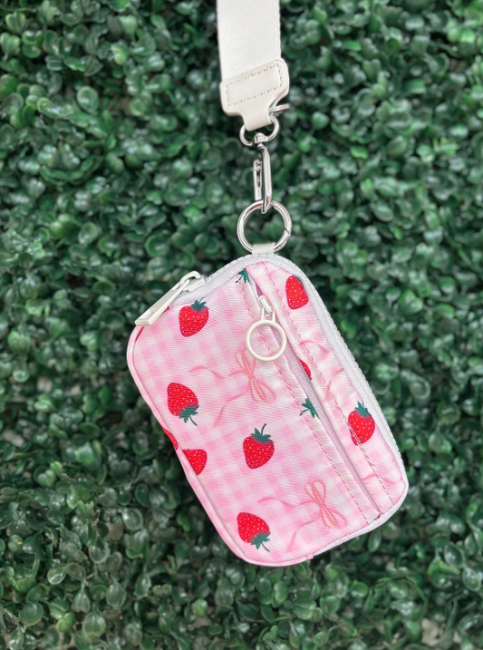 Pink pouch with strawberry pattern and white strap on green textured background