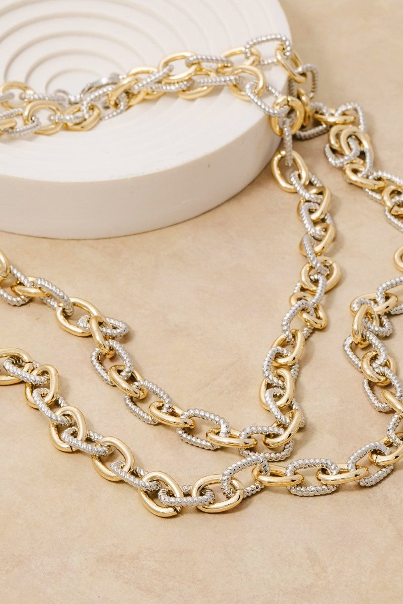 Gold and silver chain necklaces on a beige surface