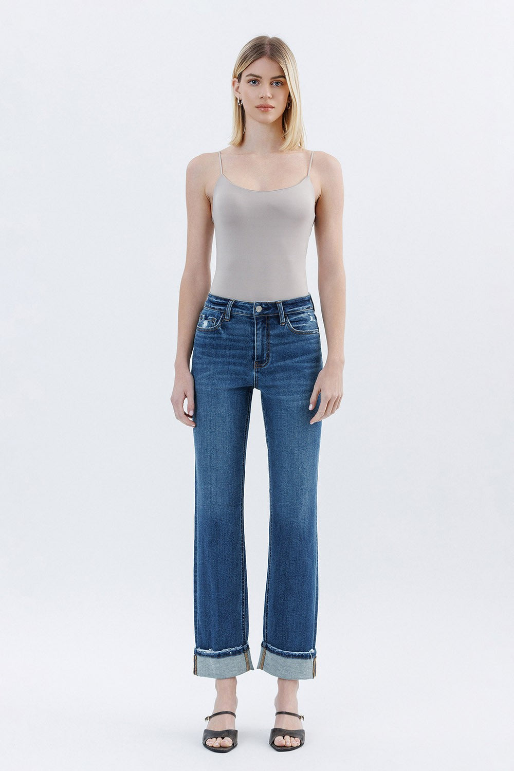 Woman wearing a beige tank top and blue jeans on a white background