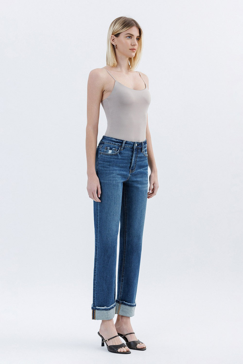 Woman wearing a beige tank top and blue jeans on a white background