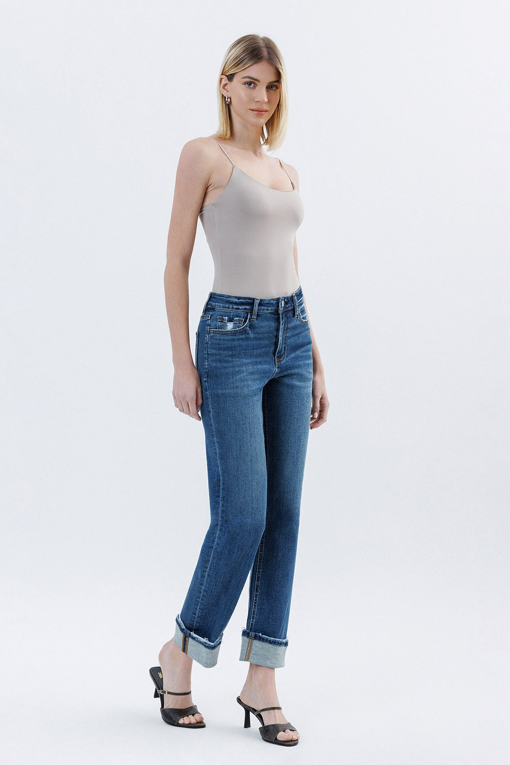 Woman wearing a light gray tank top and blue jeans on a white background