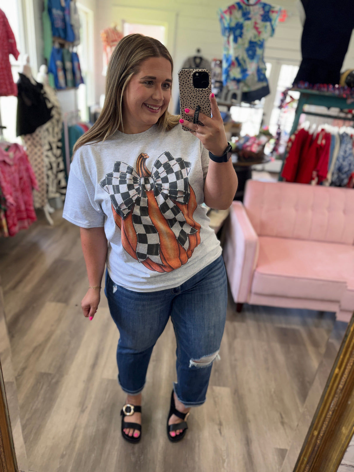 Woman taking a mirror selfie wearing a graphic t-shirt and jeans in a store.
