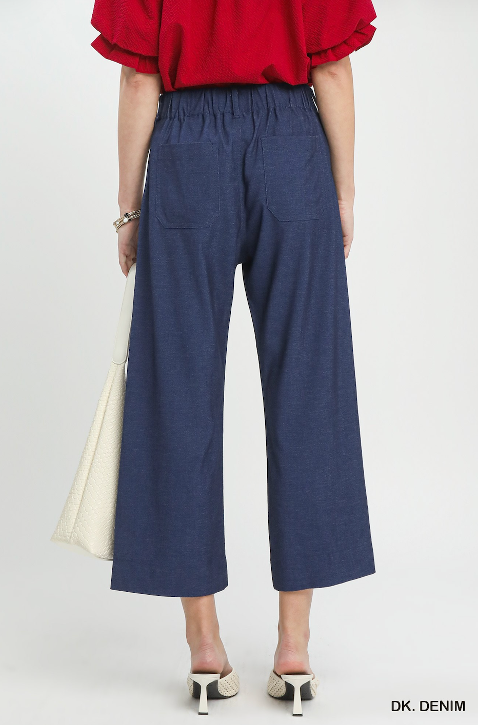 A model shown from the back wearing dark blue wide-leg cropped pants with an elastic waistband and side pockets, paired with a red top and white heels, against a light gray studio background.