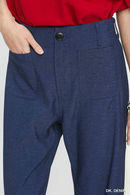 Close-up of a person wearing dark blue heathered trousers with a red top, showing the front waistband, button, side pockets, and hand in pocket against a light gray background.