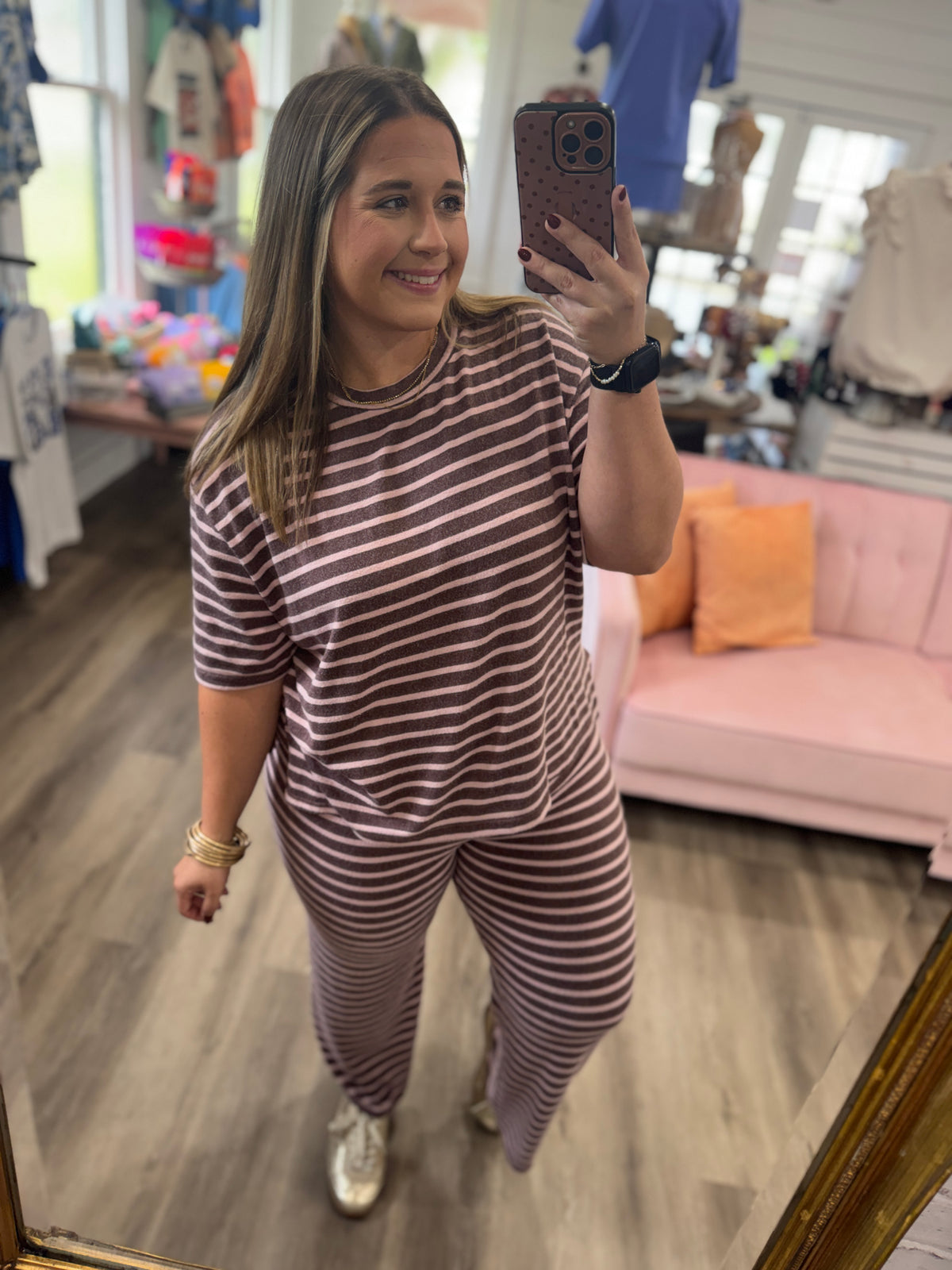 A woman takes a mirror selfie in a boutique wearing a matching short-sleeve top and pants set with horizontal brown and white stripes.