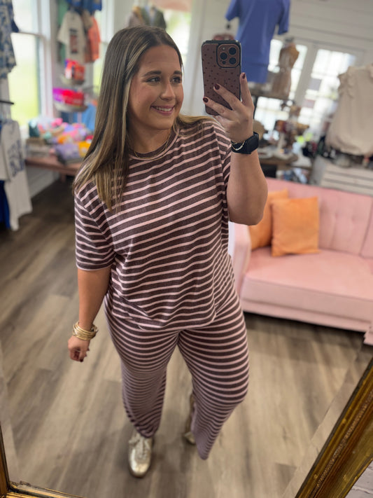 A woman takes a mirror selfie in a boutique wearing a matching short-sleeve top and pants set with horizontal brown and white stripes.