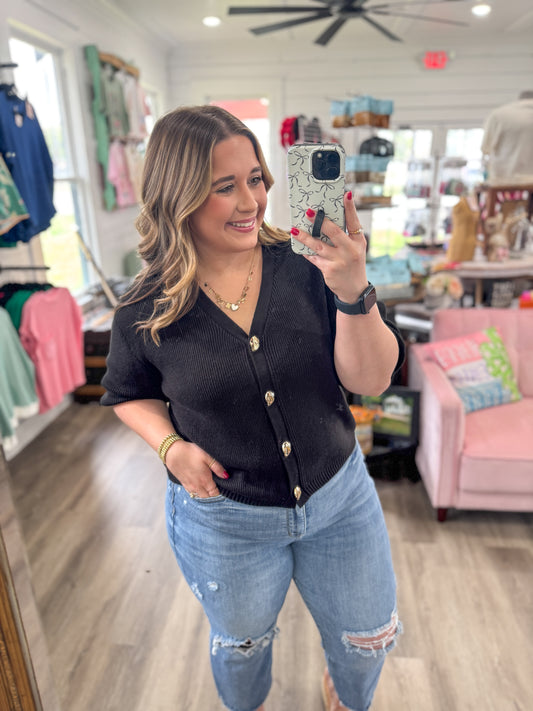 Woman taking a mirror selfie wearing a black button-up shirt and light blue jeans in a store.