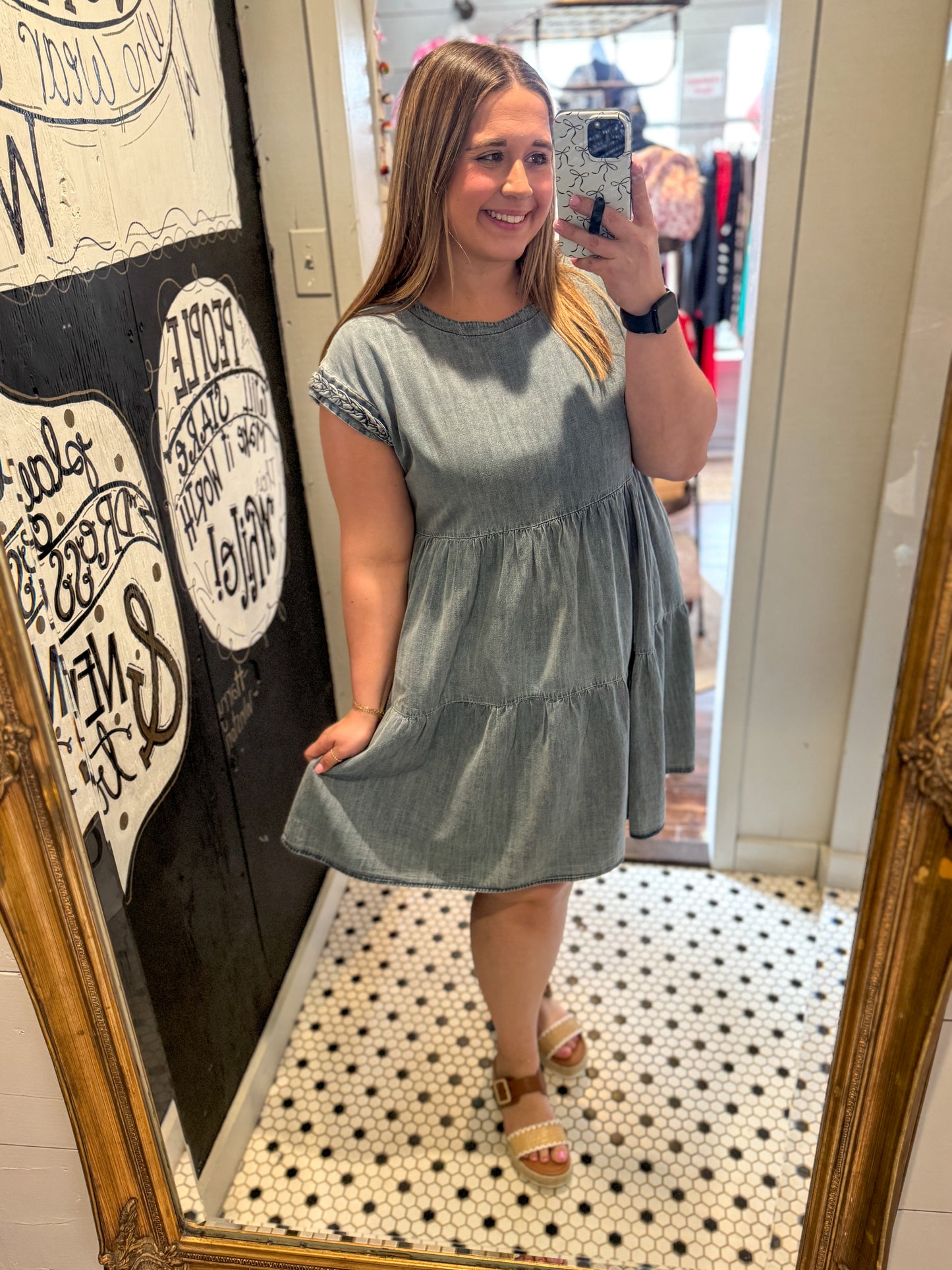 Woman taking a mirror selfie wearing a light blue dress in a store.