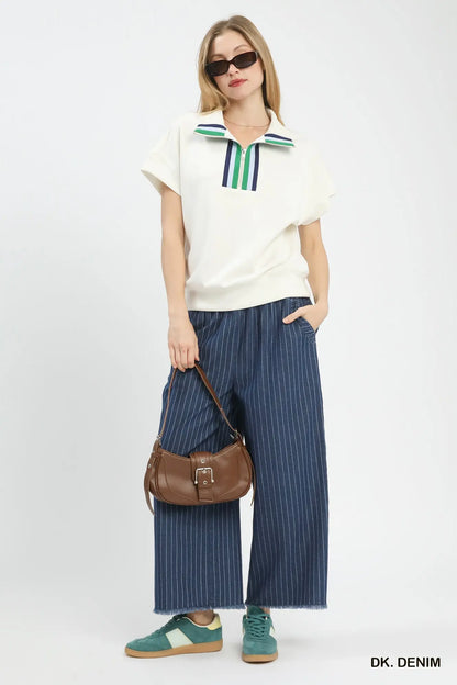 Woman wearing a white polo shirt with colorful collar and blue striped pants, holding a brown handbag on a white background.