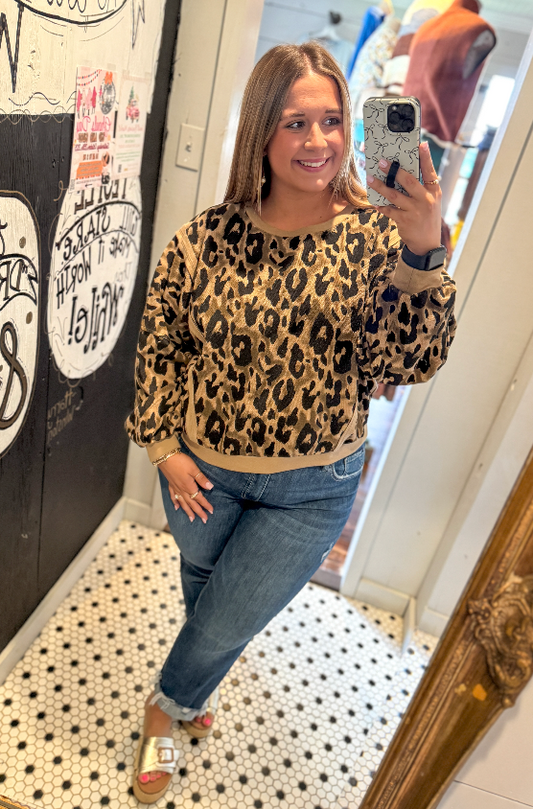 Woman taking a mirror selfie wearing a leopard print sweater and jeans.